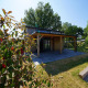 Lille lodge Tiny House Plus 4 i sollys med træterrasse, grøn have og omgivet af træer om sommeren