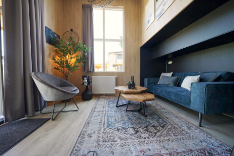 Modernes Wohnzimmer im Tiny House Plus 4 bei Zuiderzee, Niederlande, mit blauer Couch und Teppich.