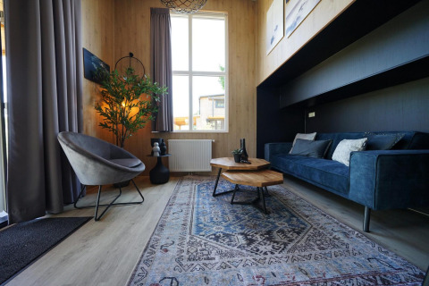 Moderne zithoek in Tiny House Plus 4 aan Zuiderzee, Nederland, met blauwe zetel en veel licht.