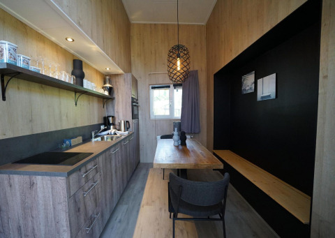 Moderne, compacte keuken en eetruimte in Tiny House Plus 4 bij Zuiderzee, Nederland, met houten interieur.