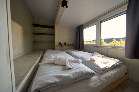 Gemütliches Schlafzimmer mit Doppelbett und großen Fenstern im Tiny House Plus 4 in Zuiderzee, Niederlande.
