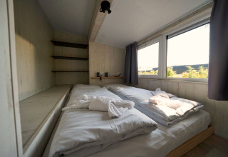 Gemütliches Schlafzimmer mit Doppelbett und großen Fenstern im Tiny House Plus 4 in Zuiderzee, Niederlande.