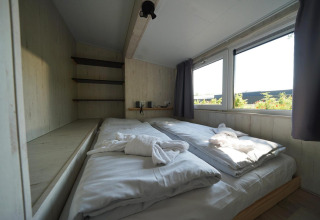 Lichte slaapkamer met tweepersoonsbed en grote ramen in Tiny House Plus 4 bij Zuiderzee, Nederland.