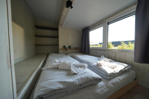 Lichte slaapkamer met dubbel bed en grote ramen in Tiny House Plus 4 te Zuiderzee, Nederland.