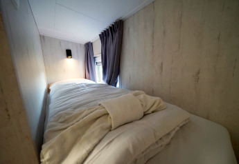 Letto singolo accogliente con lenzuola morbide e luce soffusa in Tiny House Plus 4 a Zuiderzee, Paesi Bassi.
