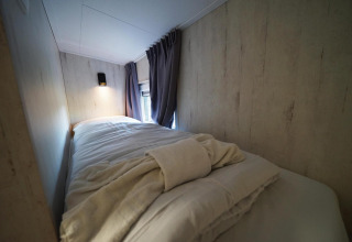 Acogedora cama individual con sábanas suaves y luz tenue en Tiny House Plus 4 en Zuiderzee, Países Bajos.