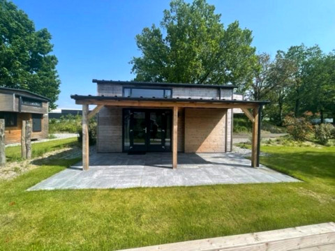 Moderne Tiny House Plus 4-Lodge mit Holzveranda in Zuiderzee, Niederlande, mit viel Grün drumherum.