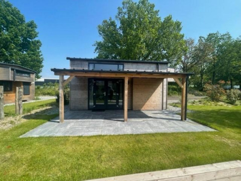 Moderne Tiny House Plus 4 lodge met houten terras bij Zuiderzee in Nederland, omgeven door groen.