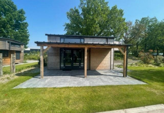 Moderne Tiny House Plus 4 lodge met houten terras bij Zuiderzee in Nederland, omgeven door groen.