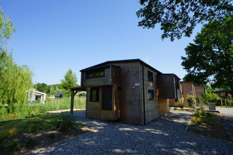 Moderne houten lodge Tiny House Plus 4 bij Zuiderzee in Nederland, omgeven door groen en blauwe lucht.