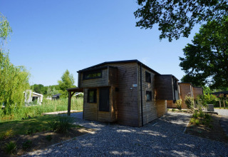 Moderne houten lodge Tiny House Plus 4 bij Zuiderzee in Nederland, omgeven door groen en blauwe lucht.