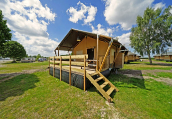 Glampingtent 6 lodge with wooden deck at a campground, surrounded by green fields and other cabins.