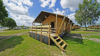 Glampingtent 6 lodge with wooden deck at a campground, surrounded by green fields and other cabins.