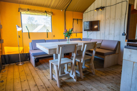 Interior de Glampingtent 6 en Zuiderzee, Países Bajos, con mesa de madera, sillas y sofá amplio.
