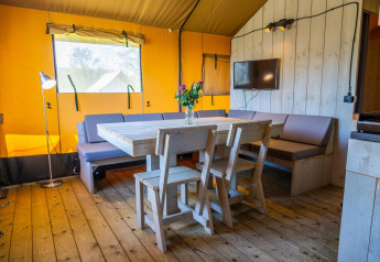 Het interieur van Glampingtent 6 bij Zuiderzee in Nederland met houten tafel, stoelen en bank.