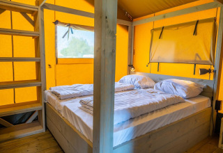 Interno di Glampingtent 6 a Zuiderzee, Paesi Bassi, con letto matrimoniale e dettagli in legno.