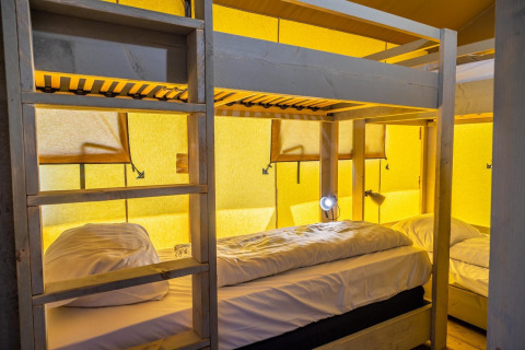 Bunk beds inside a cozy glamping tent at Zuiderzee in the Netherlands with yellow illuminated walls.