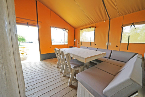 Interior of Glampingtent 6 at Zuiderzee, Netherlands, featuring wood table, seating, and canvas walls.