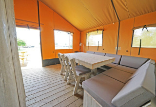 Innenraum des Glampingtent 6 in Zuiderzee, Niederlande, mit Holztisch und gepolsterten Bänken.