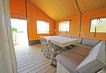 Interieur van Glampingtent 6 bij Zuiderzee, Nederland, met houten tafel en comfortabele kussenzitjes.