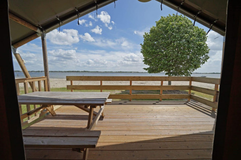 View from Glampingtent 6 at Zuiderzee in the Netherlands, with wooden deck, bench, and lakeside scenery.