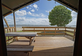 Uitzicht vanuit Glampingtent 6 bij Zuiderzee in Nederland, met houten terras, bankje en uitzicht op het meer.