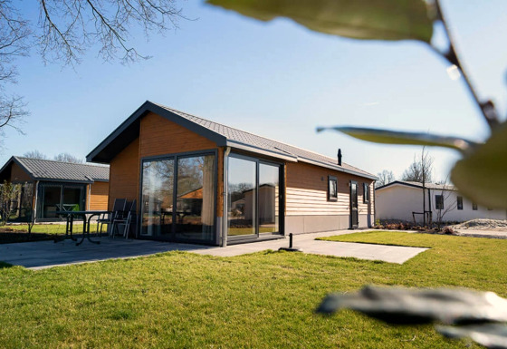 Modern lodge with large windows and a patio, surrounded by green grass and blue sky on a sunny day.