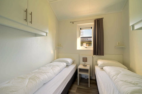 Twin bedroom with small table, window, and simple decor at Velthorst 4 lodge in Zuiderzee, Netherlands.