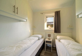 Twin bedroom with small table, window, and simple decor at Velthorst 4 lodge in Zuiderzee, Netherlands.