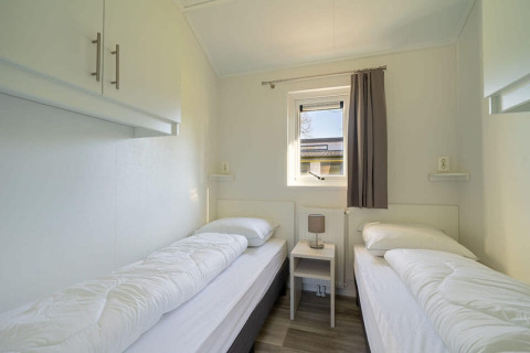 Slaapkamer met twee aparte bedden, tafeltje en venster in Velthorst 4 lodge bij Zuiderzee, Nederland.