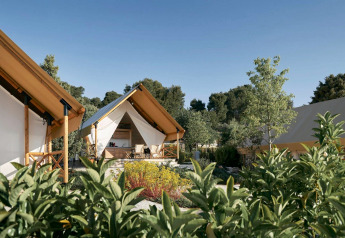 Glamping-accommodatie met luxe tenten, omgeven door groen en bomen onder een heldere hemel.