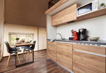 Modern glamping accommodation with a wooden kitchenette and dining table set for four people.