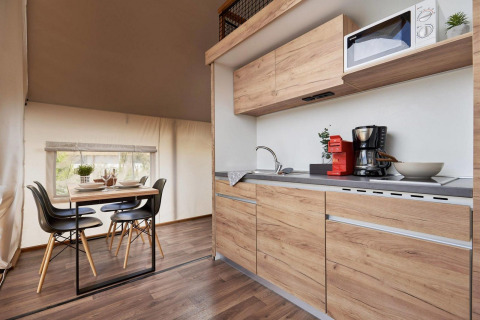 Alojamiento glamping moderno con cocina de madera equipada y mesa de comedor para cuatro personas.