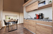 Modern glamping accommodation with a wooden kitchenette and dining table set for four people.