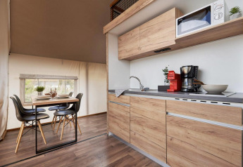 Moderne glamping-indkvartering med fuldt udstyret køkken i træ og spisebord med fire stole.