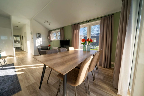 Helle Lodge mit Essbereich, großem Holztisch, sechs Stühlen, Fenstern, Vorhängen und Grünschmuck.