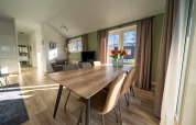 Salle à manger de lodge lumineuse avec grande table en bois, six chaises, larges fenêtres et rideaux.