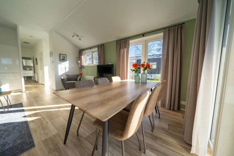 Comedor de lodge luminoso con mesa de madera, seis sillas, grandes ventanales y cortinas beige.