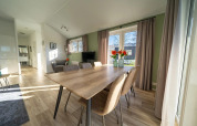 Moderne lodge med lys spisestue, store vinduer, gardiner, træbord, seks stole og grønne vægge.