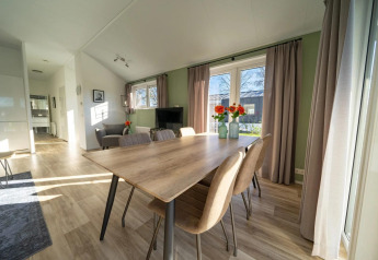 Helle Lodge mit Essbereich, großem Holztisch, sechs Stühlen, Fenstern, Vorhängen und Grünschmuck.