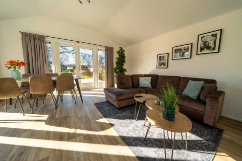 Helles, modernes Lodge-Wohnzimmer mit Ecksofa, Esstisch, großen Fenstern und Gartenblick.