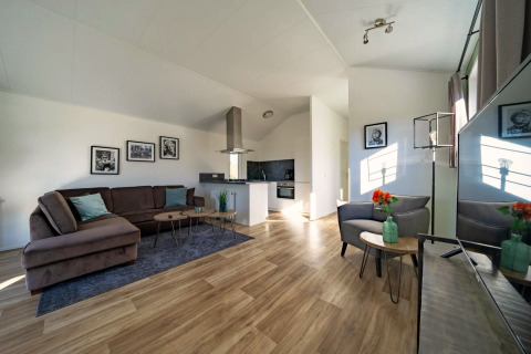Helles, modernes Wohnzimmer einer Lodge mit Ecksofa, offener Küche und Holzboden, dekoriert mit Kunst.