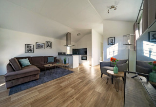 Helles, modernes Wohnzimmer einer Lodge mit Ecksofa, offener Küche und Holzboden, dekoriert mit Kunst.