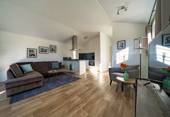 Luminoso soggiorno di un lodge moderno con divano angolare, cucina aperta, pavimento in legno e decorazioni.
