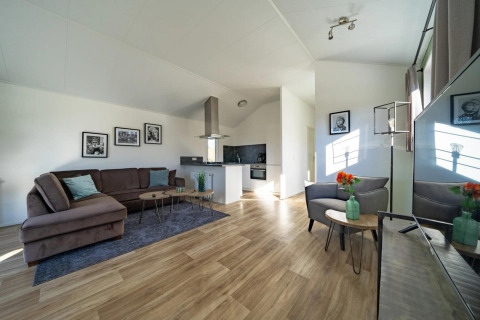 Salon de lodge lumineux et moderne avec canapé d'angle, cuisine ouverte, parquet et œuvres d'art murales.