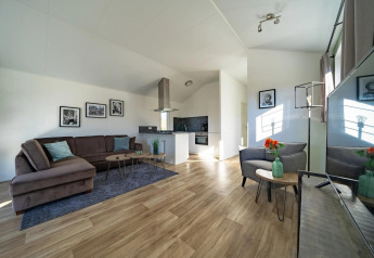 Heldere, moderne lodge woonkamer met zitbank, open keuken, houten vloer en kunstwerken aan de muur.