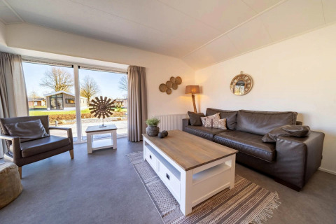 Helles, modernes Wohnzimmer in einer Lodge mit großen Fenstern, Ledersofa, Sessel und Naturblick.
