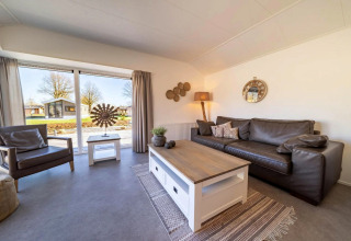 Helles, modernes Wohnzimmer in einer Lodge mit großen Fenstern, Ledersofa, Sessel und Naturblick.