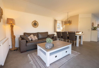 Sala de estar en lodge con sofá marrón, mesa de centro blanca, comedor y decoración rústica.