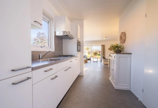 Cabaña moderna con cocina luminosa en primer plano y acogedora sala de estar con ventanales al fondo.